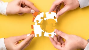 hands holding puzzle pieces together with orange pegs logo on the pieces