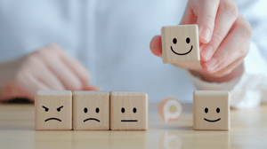 Line of blocks with faces, a man picking up the smiling face at the end and revealing an Orange Pegs logo